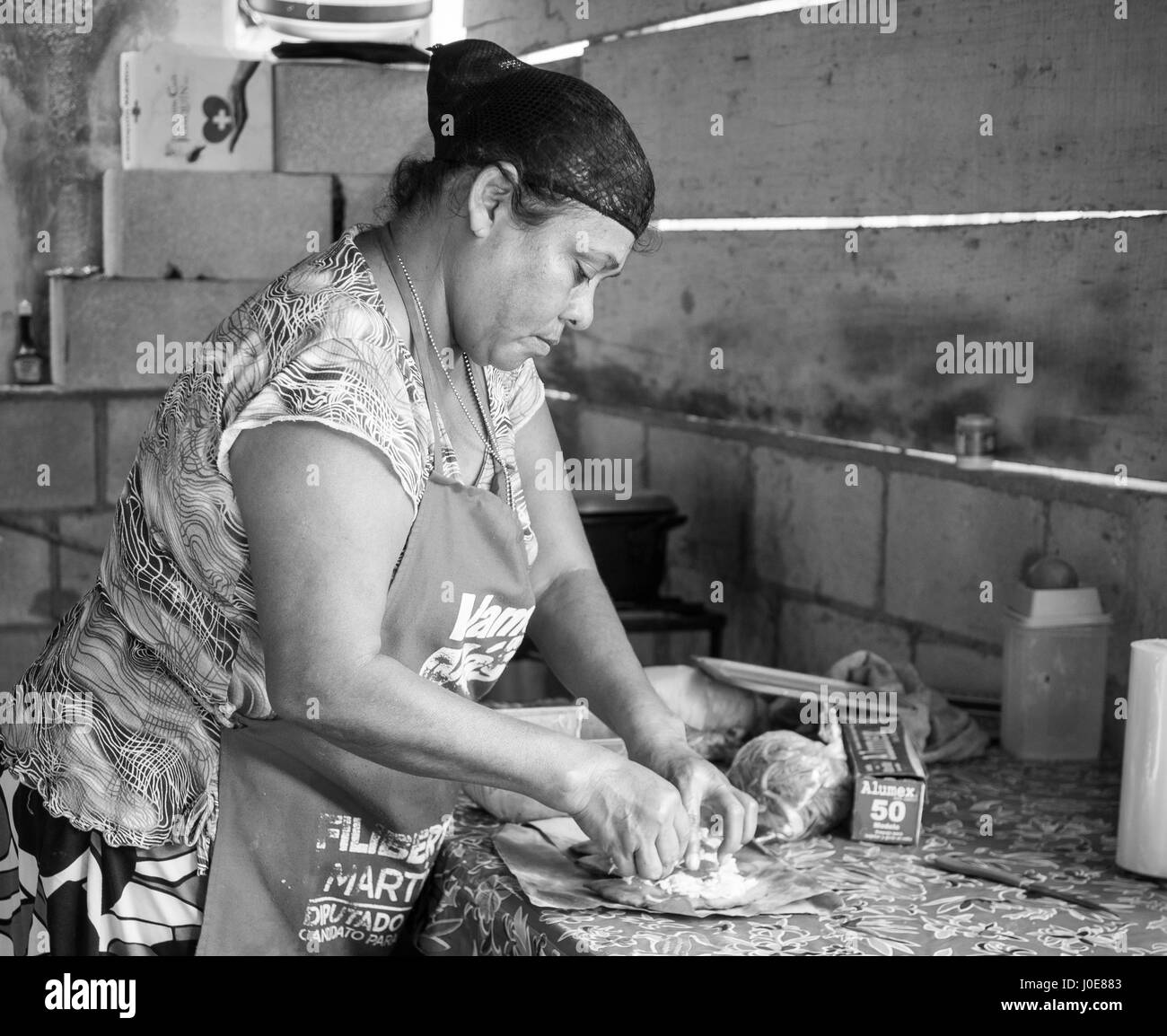 Préparation du déjeuner monochrome. Une femme prépare un dîner de rue en remplissant une tortilla avec de la salade et le poulet dans une petite cuisine approximative sur une rue secondaire o Banque D'Images
