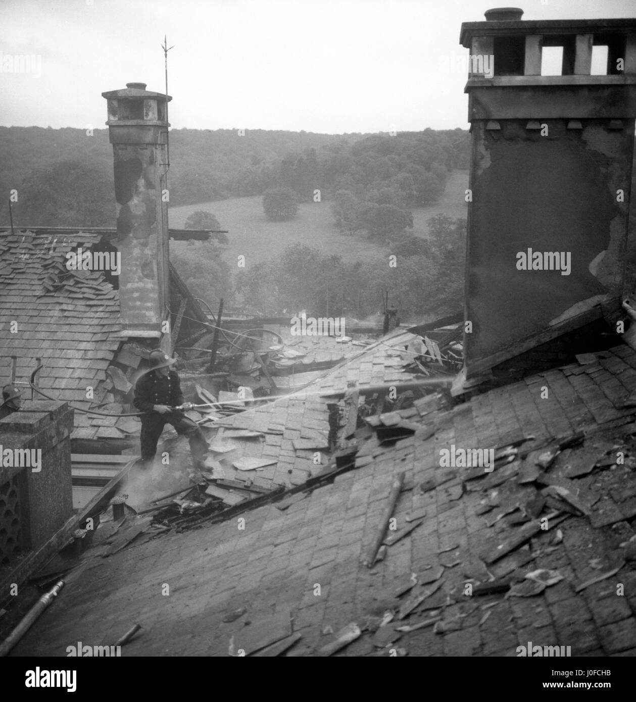 Un pompier dirige un jet d'eau à la base de la cheminée près de l'endroit où un incendie a éclaté dans le toit de Polesden Lacey, près de Dorking, Surrey. Banque D'Images
