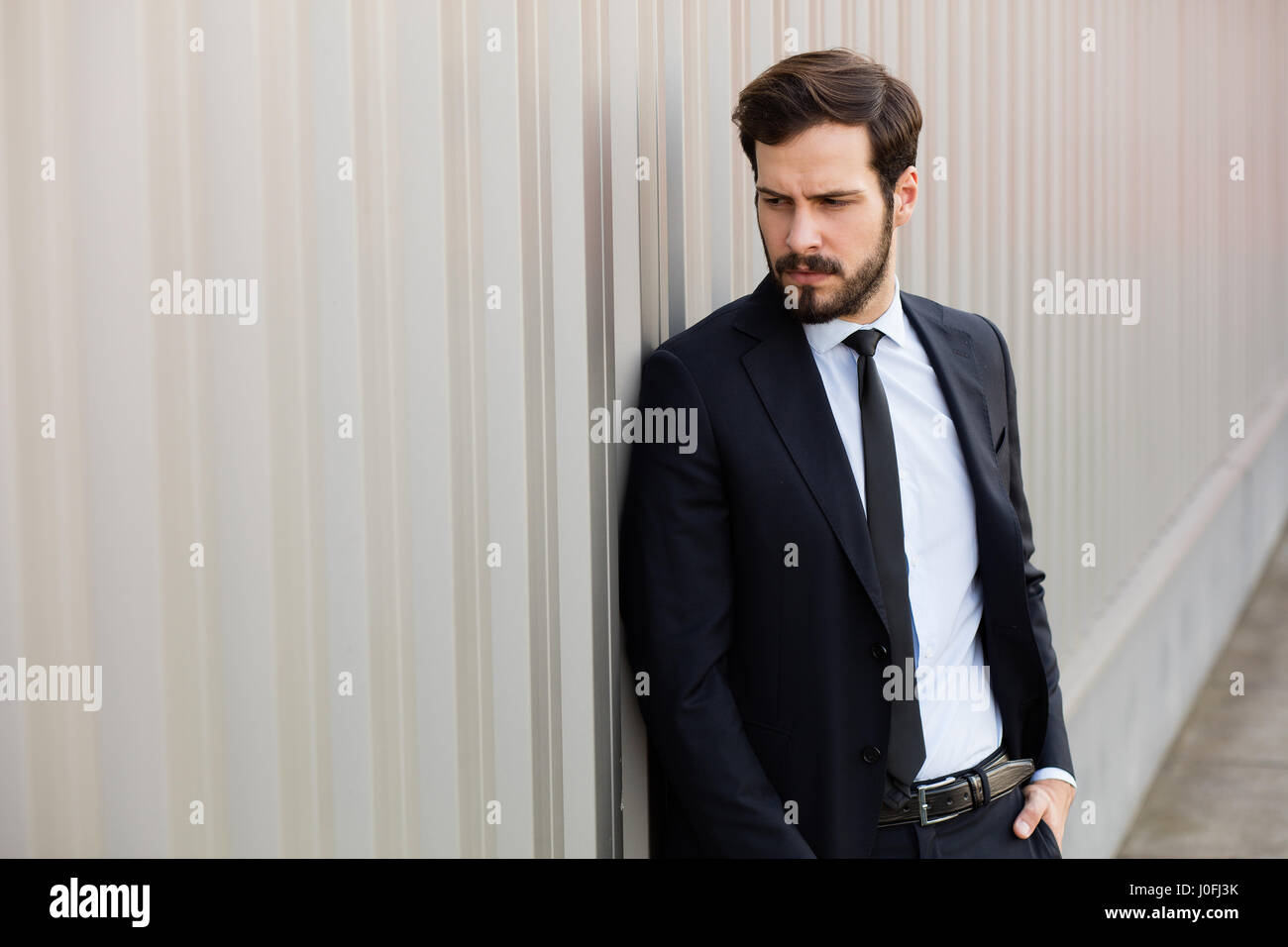 Bel homme masculin avec barbe portant costume élégant près d'un mur à l'extérieur gris Banque D'Images