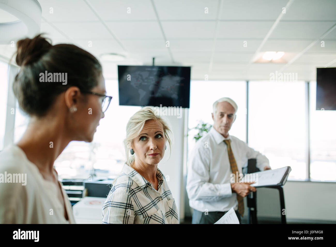 Femme mature t'écoute avec son collègue homme debout en arrière-plan. Les gens d'affaires ayant une réunion informelle dans un bureau moderne. Banque D'Images