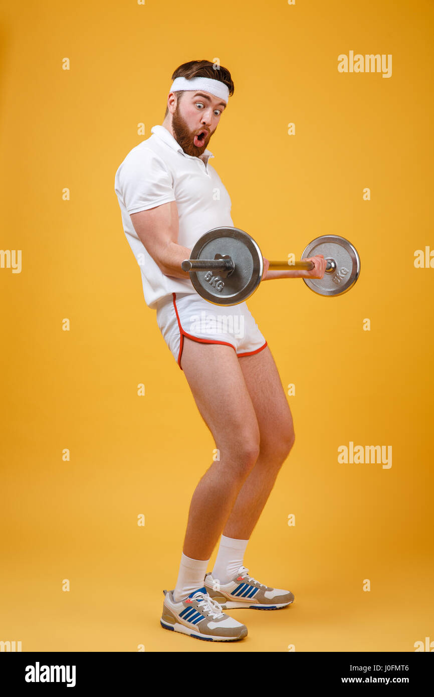 Portrait d'un jeune homme barbu fitnes faisant l'entraînement avec haltères lourds isolé sur un fond orange Banque D'Images