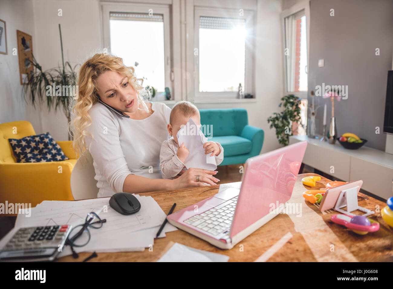 Inquiets mother holding baby et parler sur smart phone at home office Banque D'Images