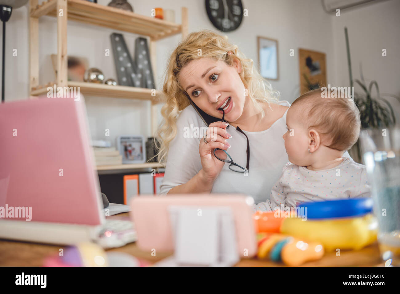 Mother holding baby, talking on smart phone at home office and using laptop Banque D'Images