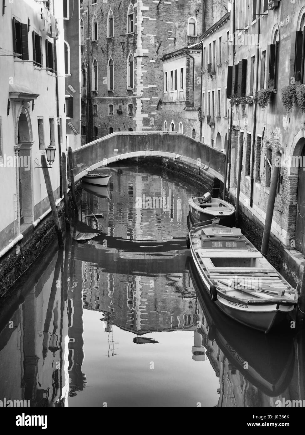 Petit pont traversant un canal à Venise avec les bots et les réflexions de la construction Banque D'Images