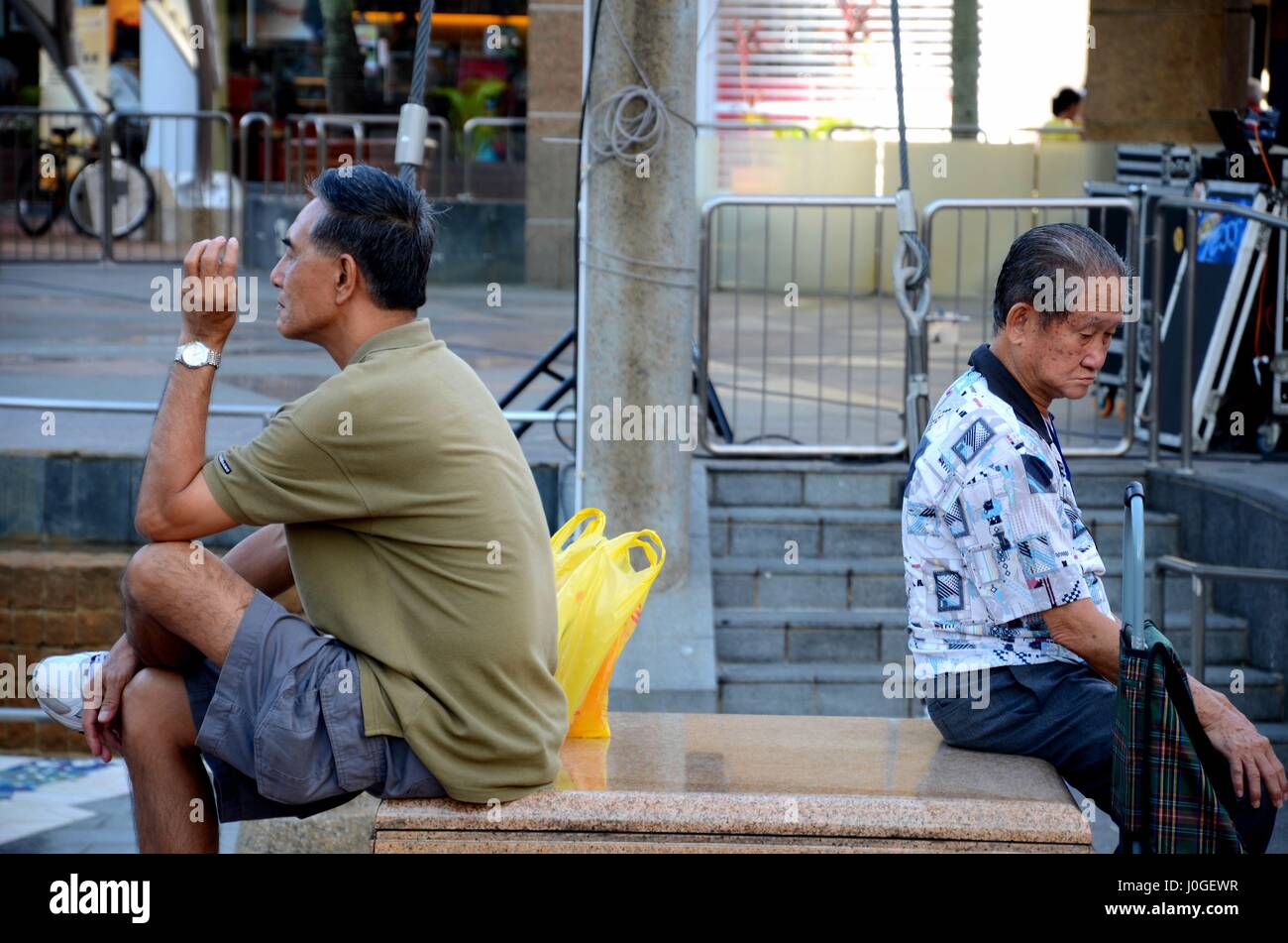 Deux hommes s'asseoir dos à dos alors que l'on fume une cigarette dans une place publique à Singapour Toa Payoh HDB estate Banque D'Images