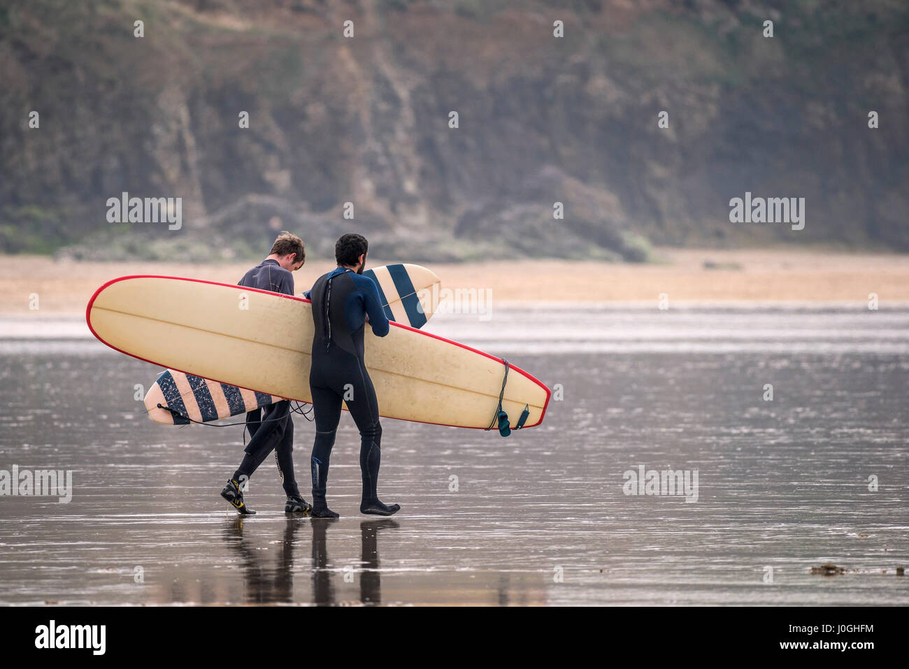 Gwithian Towans beach deux surfeurs hommes marcher dans la mer la mer transportant des planches de l'autre activité de loisirs vacanciers Longboards côtières Banque D'Images