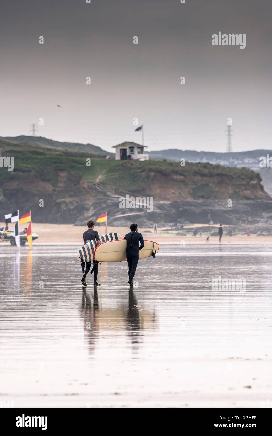 Gwithian Towans beach deux surfeurs hommes marcher dans la mer la mer transportant des planches de l'autre activité de loisirs vacanciers Longboards côtières Banque D'Images