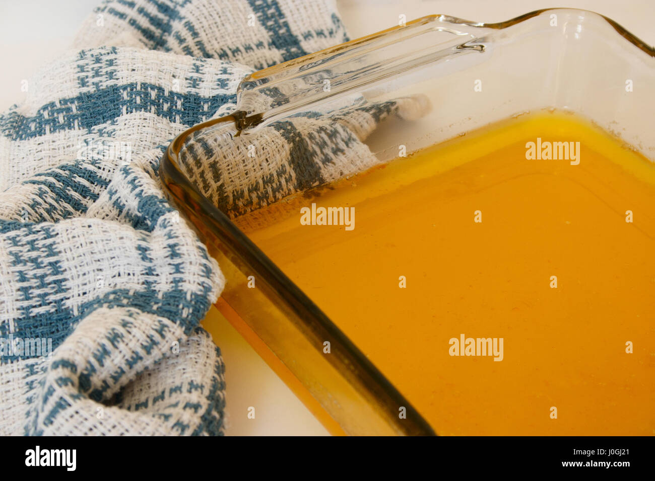 Ghee liquide dans le plat de cuisson en verre sur fond blanc avec des essuie-tout blanc-bleu Banque D'Images