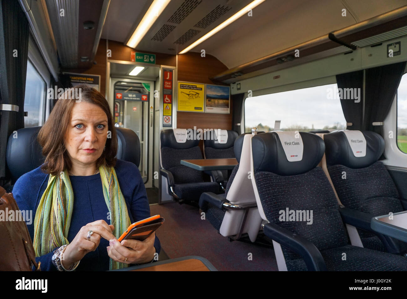Une femme d'âge moyen assis en première classe dans un train à l'aide de son téléphone portable Banque D'Images