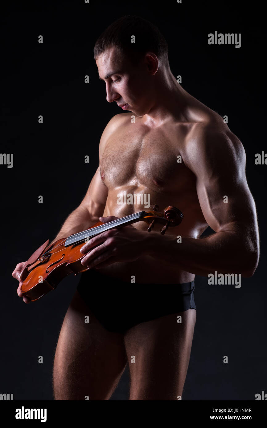 Avec de grands muscles bodybuilder tenant un petit violon dans les mains de la démonstration de grâce de l'organisme. Banque D'Images