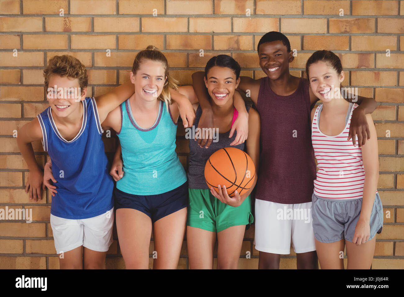 Heureux les enfants de l'école secondaire avec les bras autour de appuyé contre le mur en basket-ball Banque D'Images