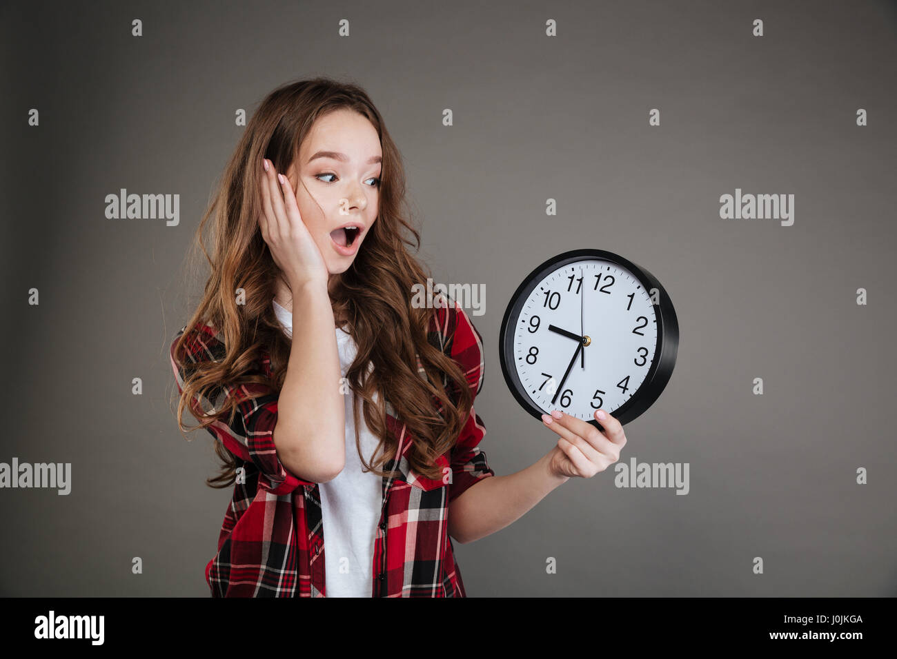 Image of young lady isolés sur fond gris holding clock. À côté. Banque D'Images