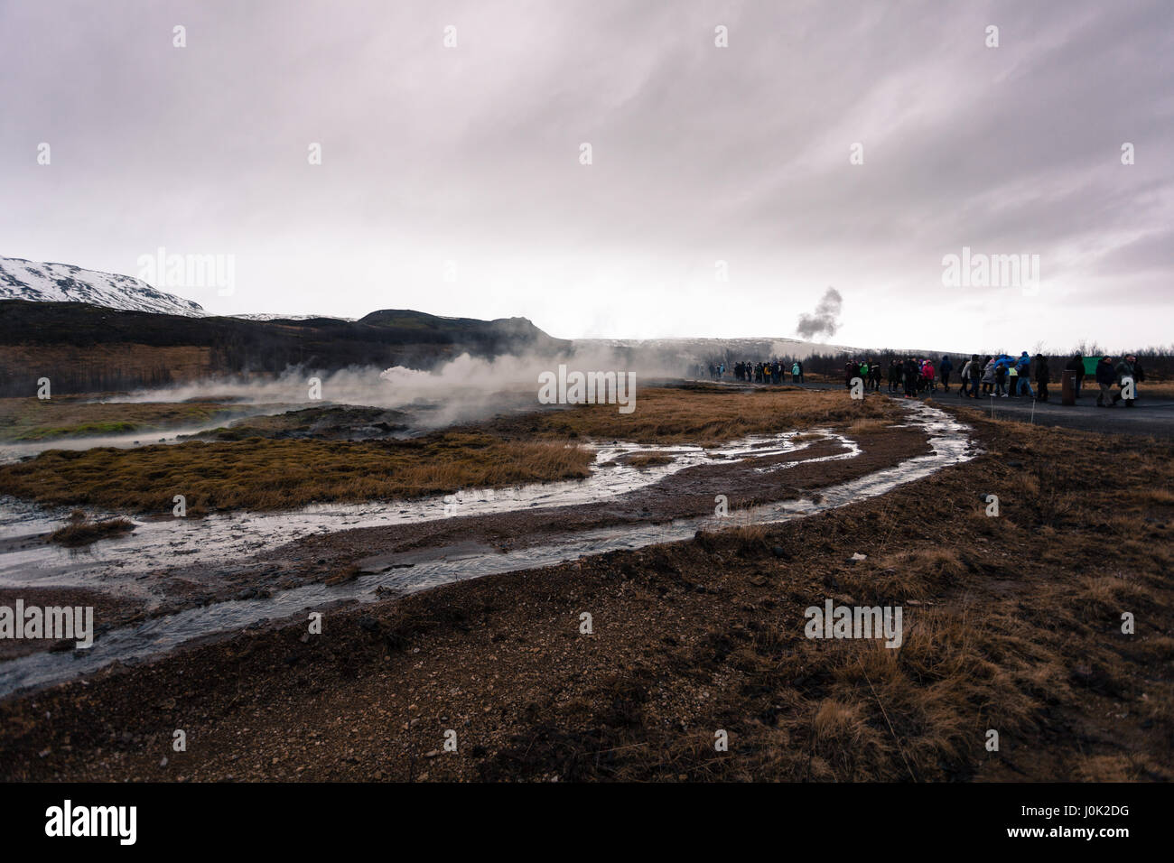 Un panache de vapeur s'élève de un printemps chaud géothermique comme une foule de touristes à pied vers les geysers. Cercle d'or, dans l'ouest de l'Islande Banque D'Images