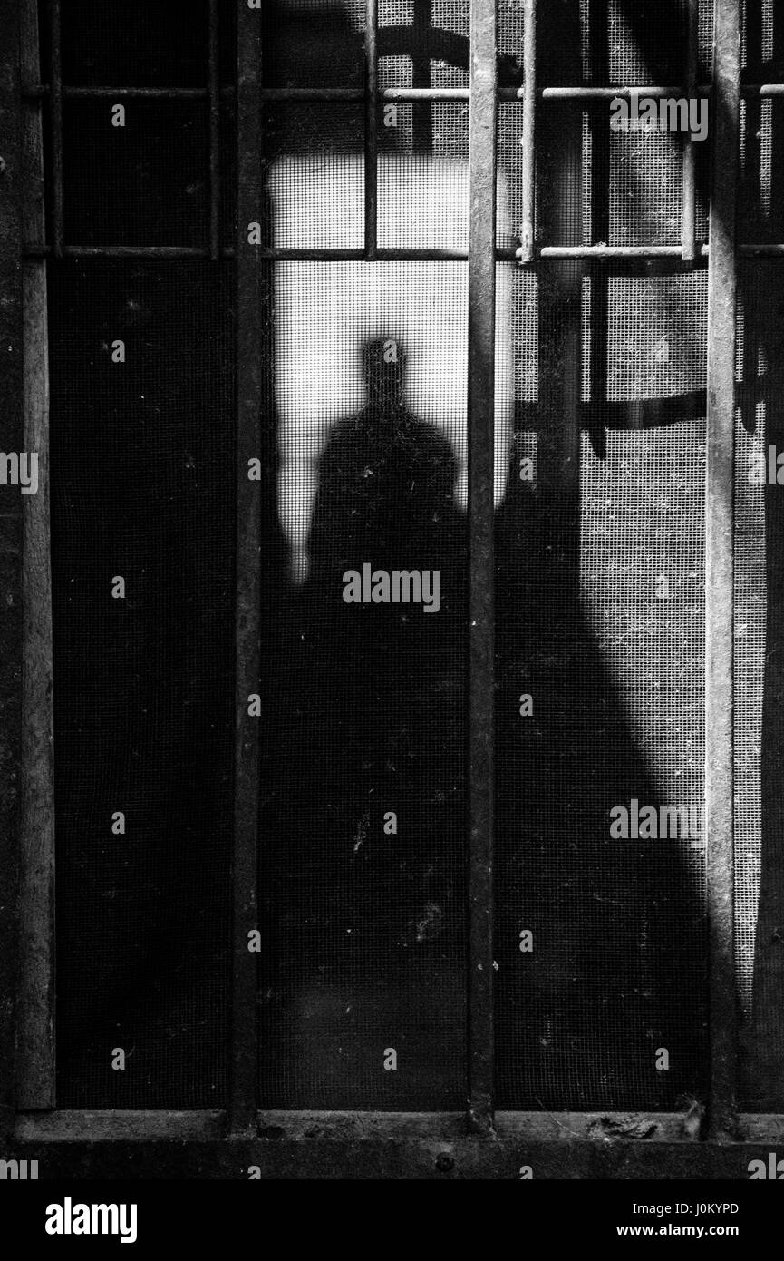 L'homme qui se profile dans l'ombre par le biais d'un écran rouillé porte. Banque D'Images