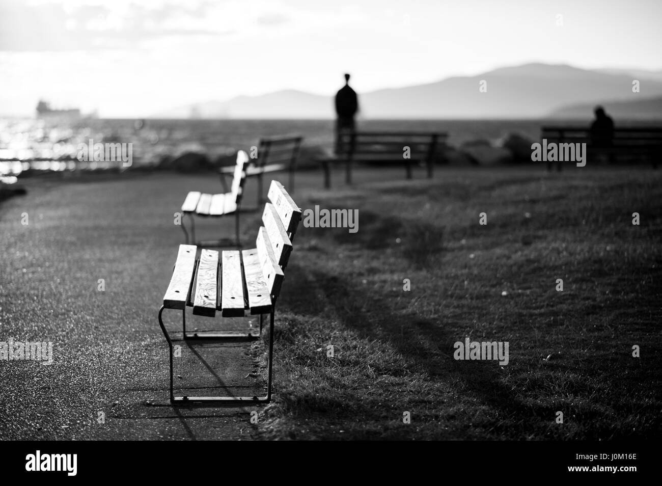 Un blurrred silhouetté homme debout debout les yeux dans l'océan, l'autre sur un banc. Banque D'Images