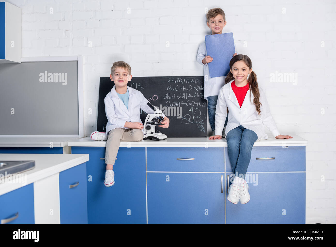 Deux petits garçons et filles en blouse blanche assis sur table en laboratoire chimique Banque D'Images