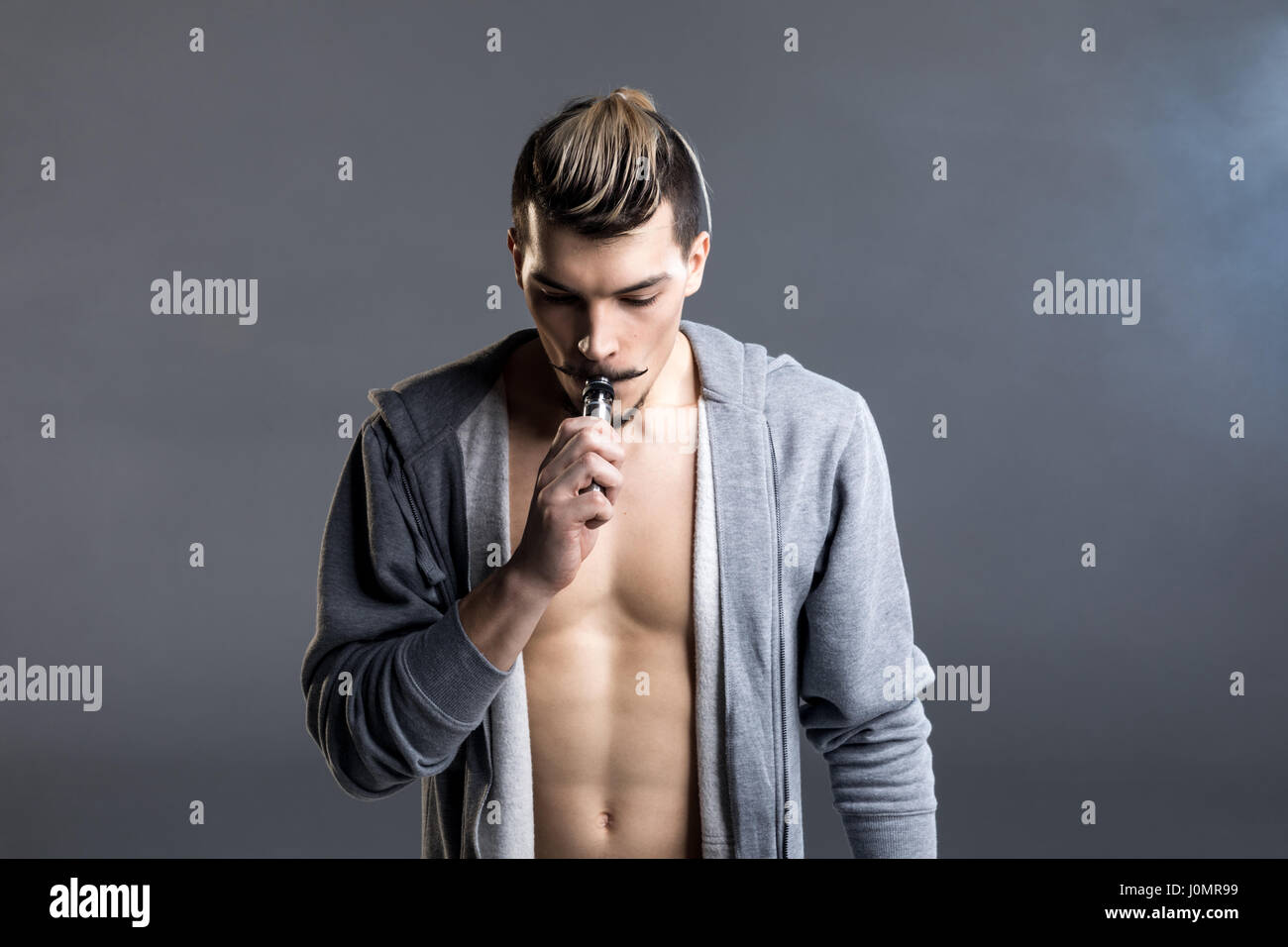 Young handsome man holding cigarette électronique et vaping sur gris Banque D'Images