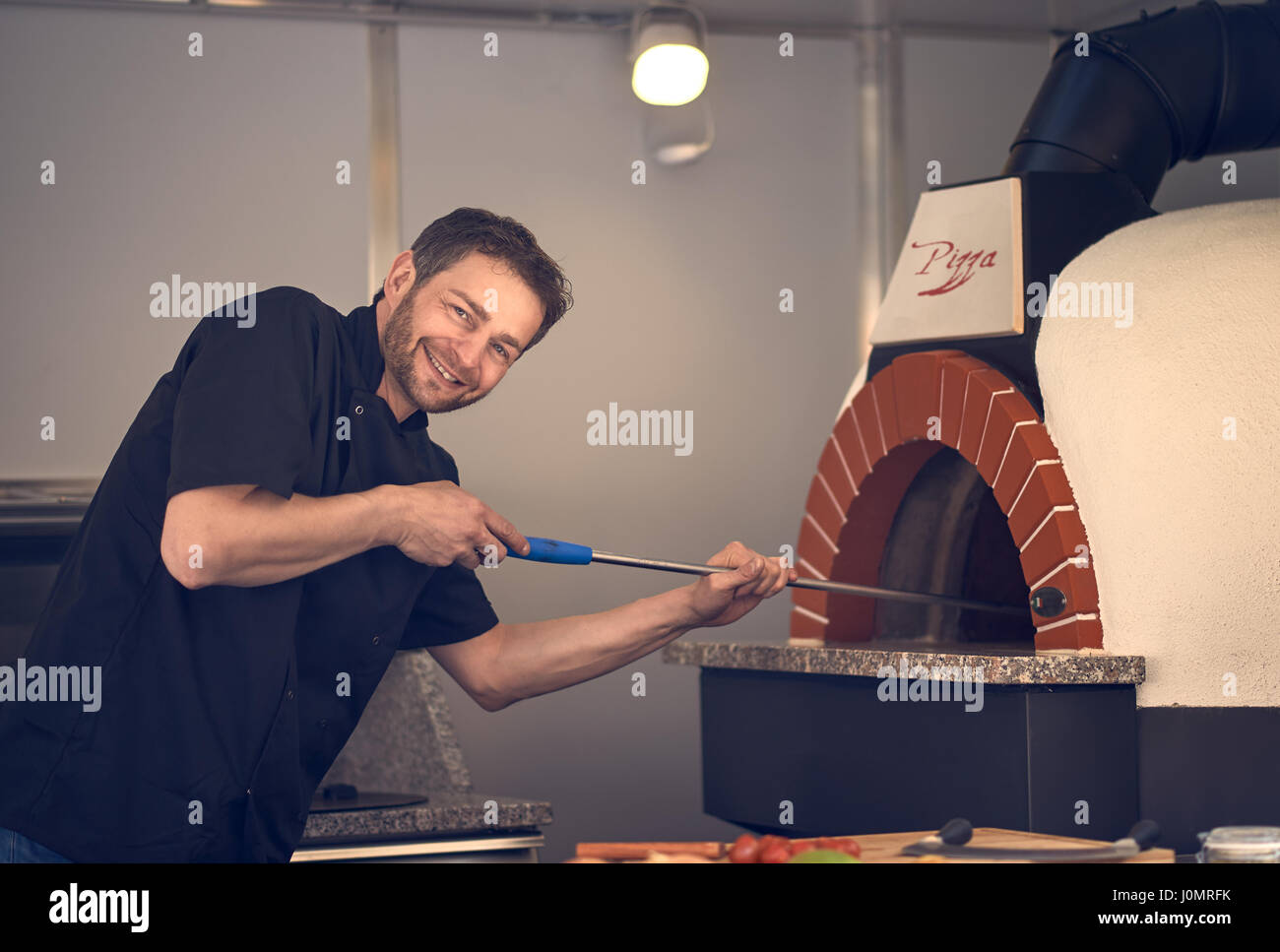 Smiling chef cuisson ou cuisson flamme une pizza italienne dans un four à bois moderne une pizzeria Banque D'Images