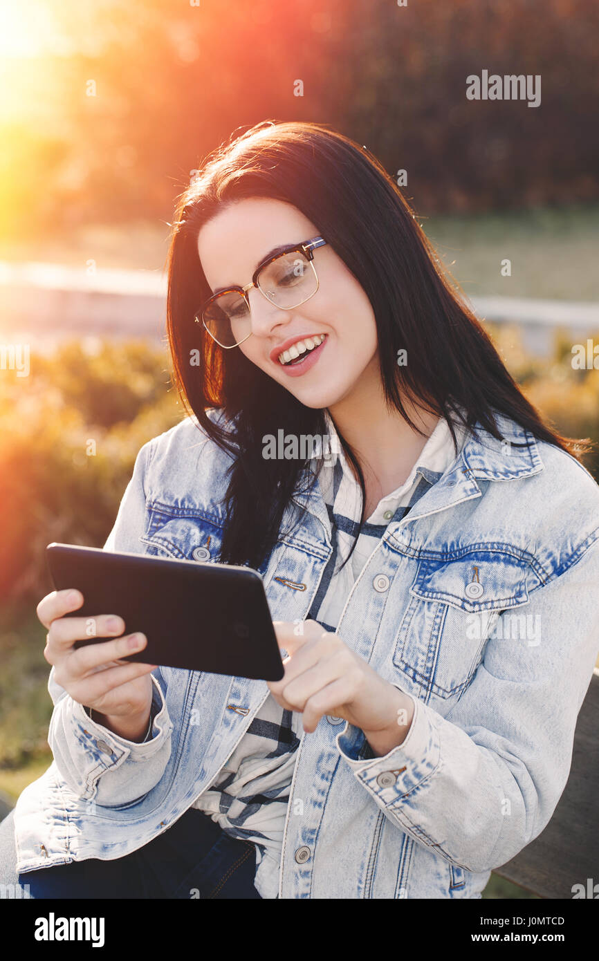 Jeune femme brune intelligente dans l'aide de lunettes de soleil en plein air comprimé Banque D'Images