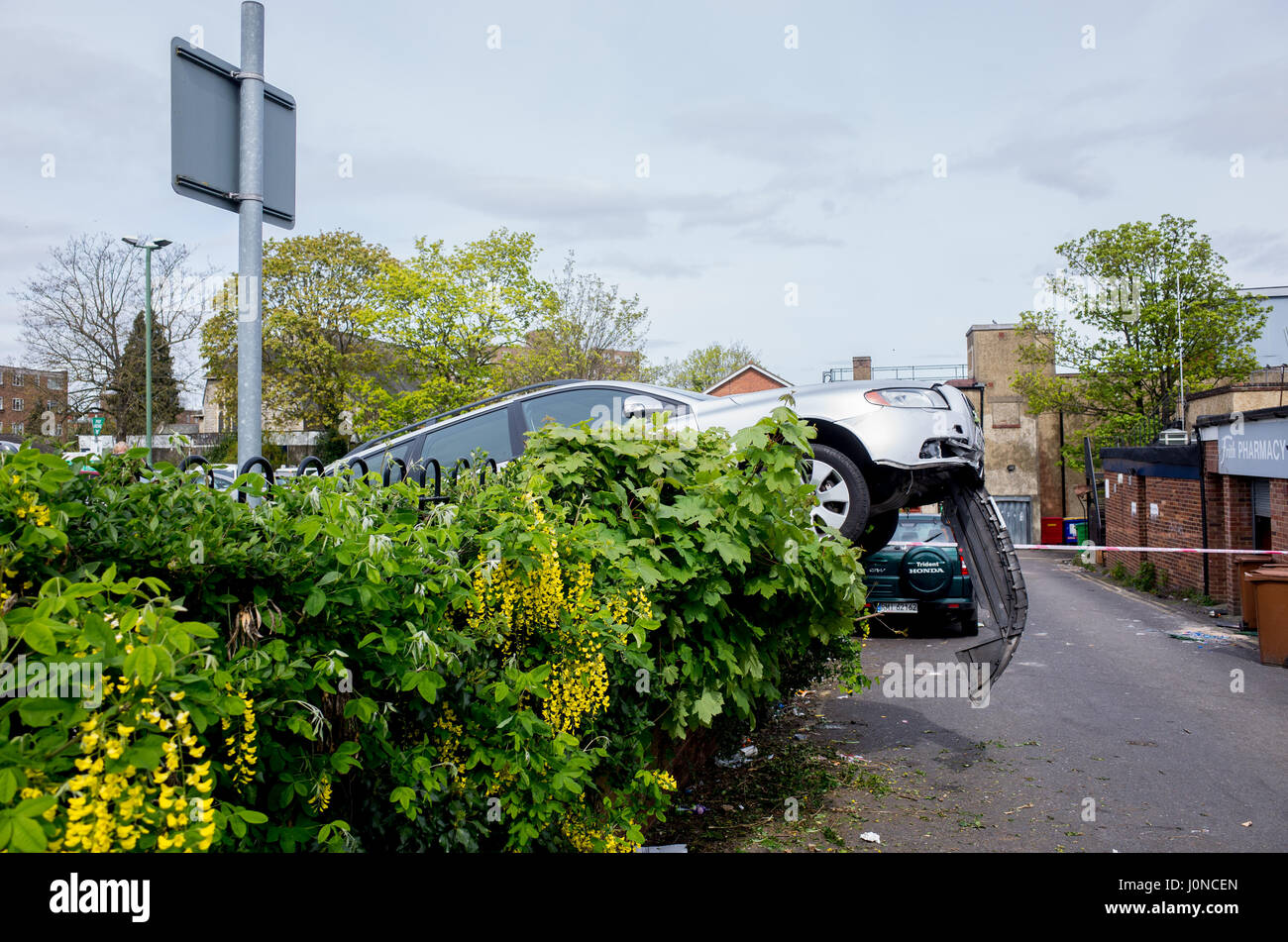 Wallington, Surrey, UK. 15 avril, 2017. Une voiture s'est écrasé à travers une haie dans Shotfied dans parking à Wallington, Surrey. L'extrémité avant se bloque plus procariously une voie de service à l'arrière de boutiques. C'est pas clair si la voiture a perdu le contrôle ou a été délibérément s'est écrasé après avoir été volés. La police étaient présents. Samedi 15 avril 2017. Wallington, London Borough of Sutton. Crédit : Darren Lehane/Alamy Live News Banque D'Images