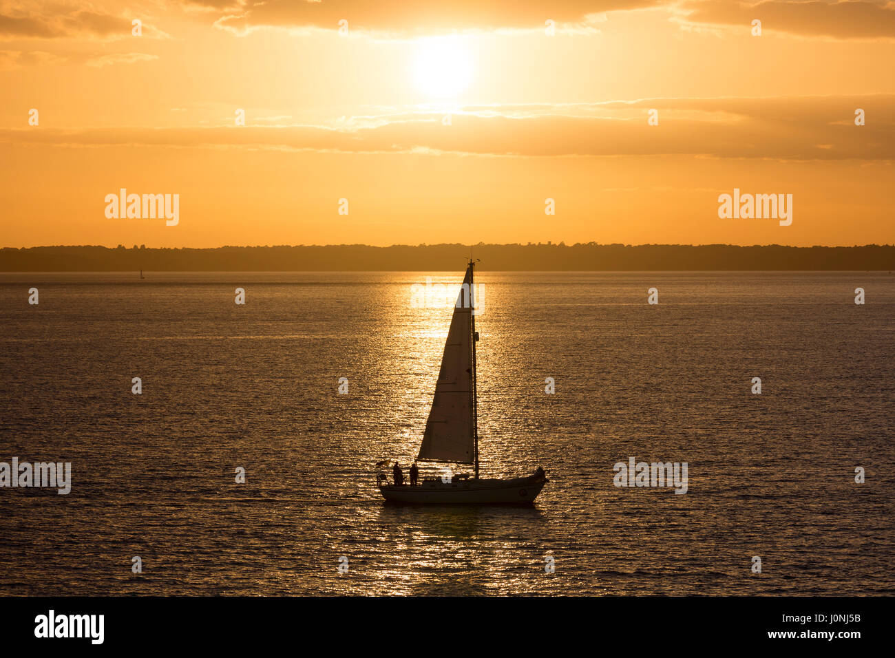 Bateau à voile solitaire en mer au coucher du soleil par la rivière Solent, UK Banque D'Images