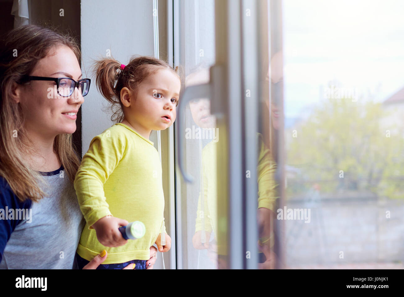 Une famille heureuse. Petite fille regarde par la fenêtre avec mère Banque D'Images