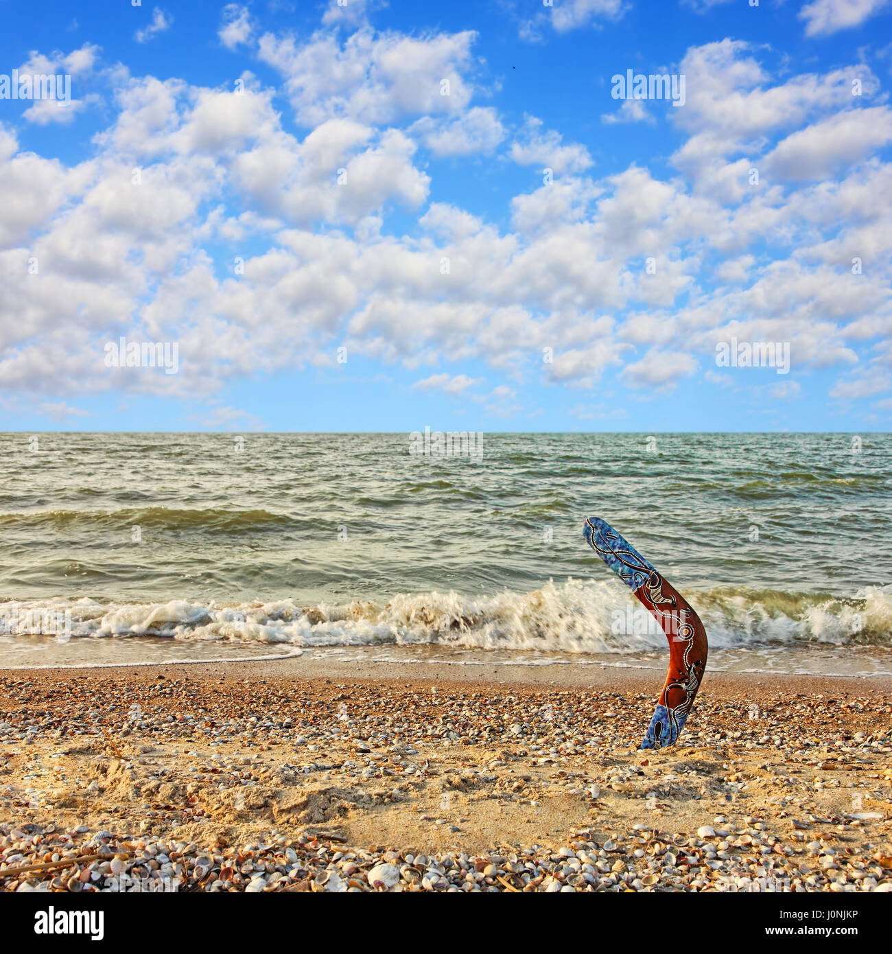Boomerang australien multicolores sur la plage de sable contre la mer de surf et ciel nuageux. Banque D'Images