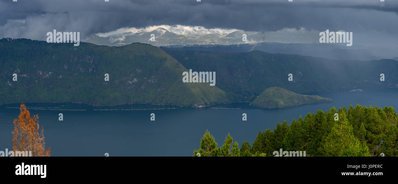 Un écart de quelques nuages sombres révèlent un lointain de montagnes. Lac Toba, au nord de Sumatra, en Indonésie. Banque D'Images