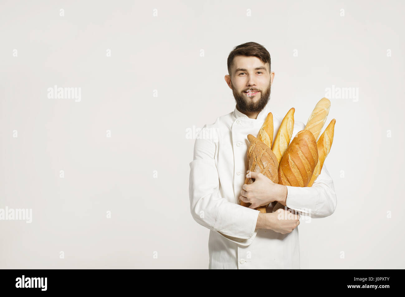 Beau Baker en uniforme la tenue des baguettes de pain avec des étagères sur le fond blanc. Handsome man holding du pain chaud dans ses mains sur white Banque D'Images