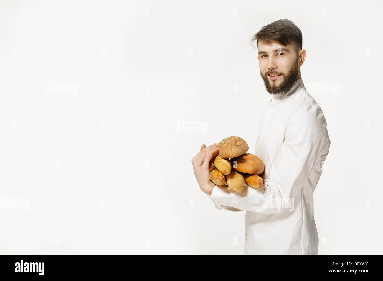 Beau Baker en uniforme la tenue des baguettes de pain avec des étagères sur le fond blanc. Handsome man holding du pain chaud dans ses mains sur white Banque D'Images