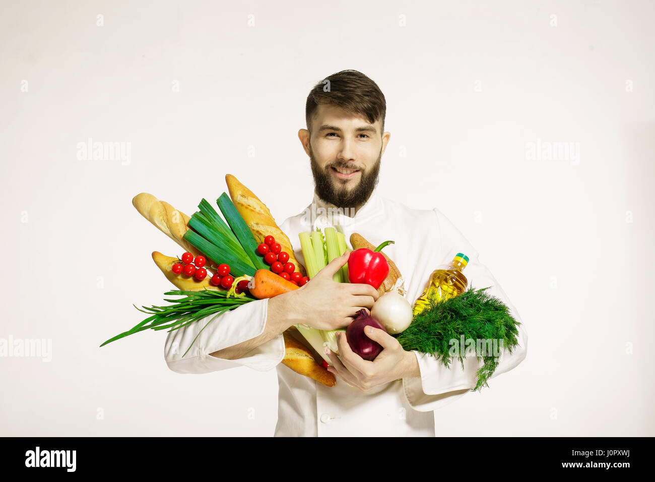 Smiling handsome chef avec des légumes en mains isolé sur fond blanc. La nourriture végétalienne. Portrait of happy chef professionnel avec légumes et fines herbes Banque D'Images