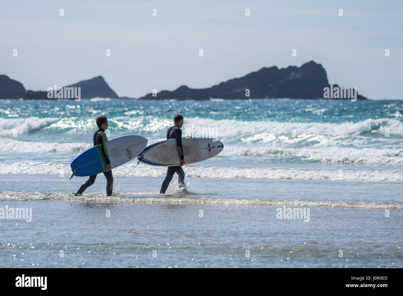 UK surf plage de Fistral Newquay Surfers marcher dans la mer transportant des planches de surf Watersport tourisme balnéaire Plage Vacances Locations Banque D'Images