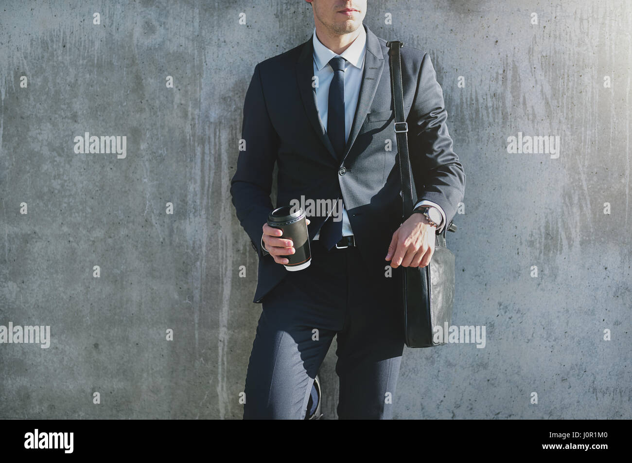 Businessman standing contemporain élégant au gray mur et tenant une tasse de café. Banque D'Images
