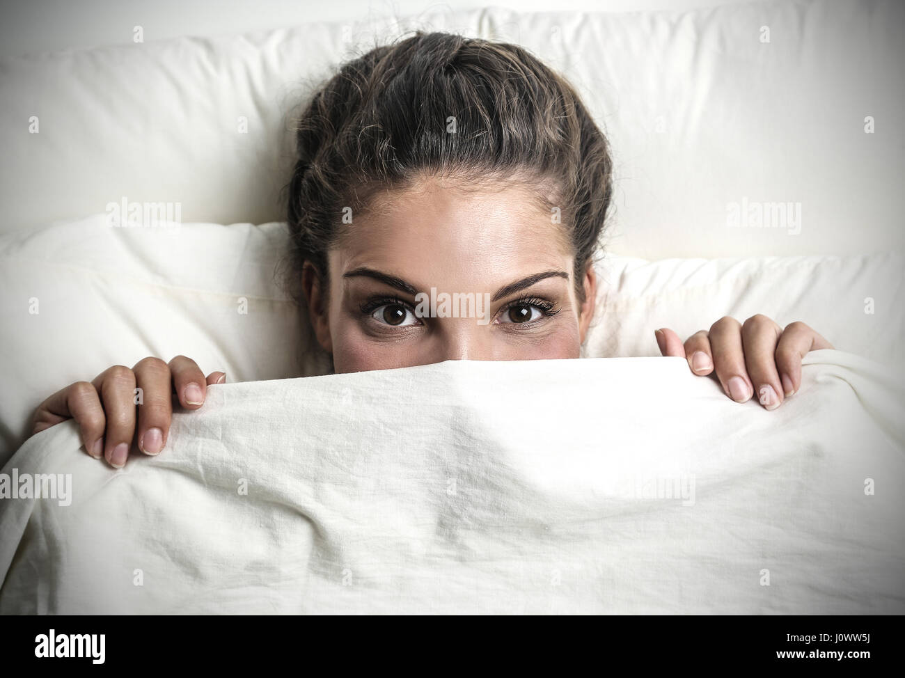 Brunette woman se cacher sous les draps Photo Stock - Alamy