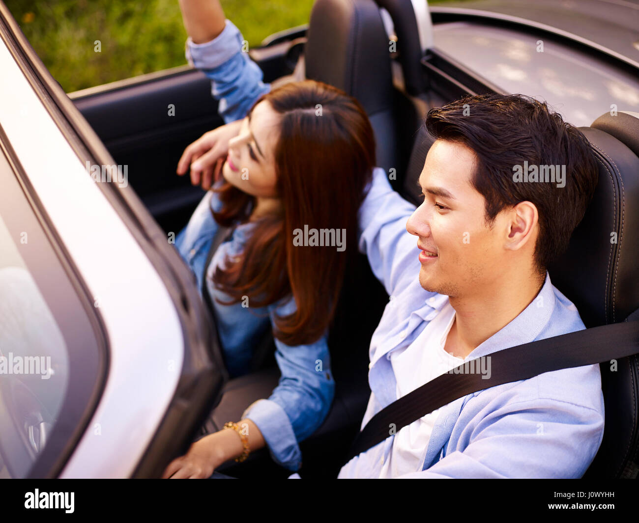 Young Asian couple riding dans un cabriolet sport car au coucher du soleil, high angle view. Banque D'Images