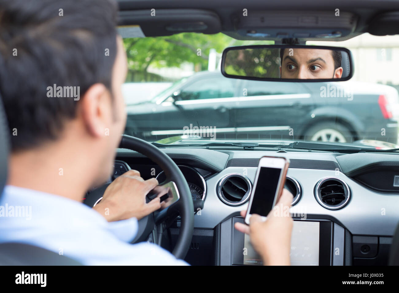 Closeup portrait, jeune homme en polo bleu roulant en voiture noire et contrôler son téléphone, puis choqué presque sur d'avoir un accident de la circulation, l'isolat Banque D'Images