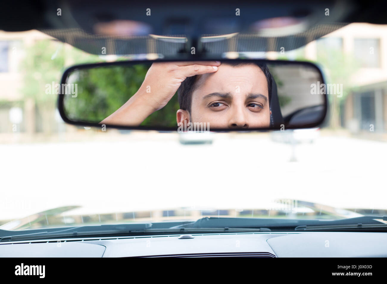 Closeup portrait drôles, jeune homme à la recherche du pilote à l'arrière, rétroviseur intérieur à la perte de cheveux au sommet de veuve questions ou de l'inquiétude, de l'intérieur windsh isolés Banque D'Images