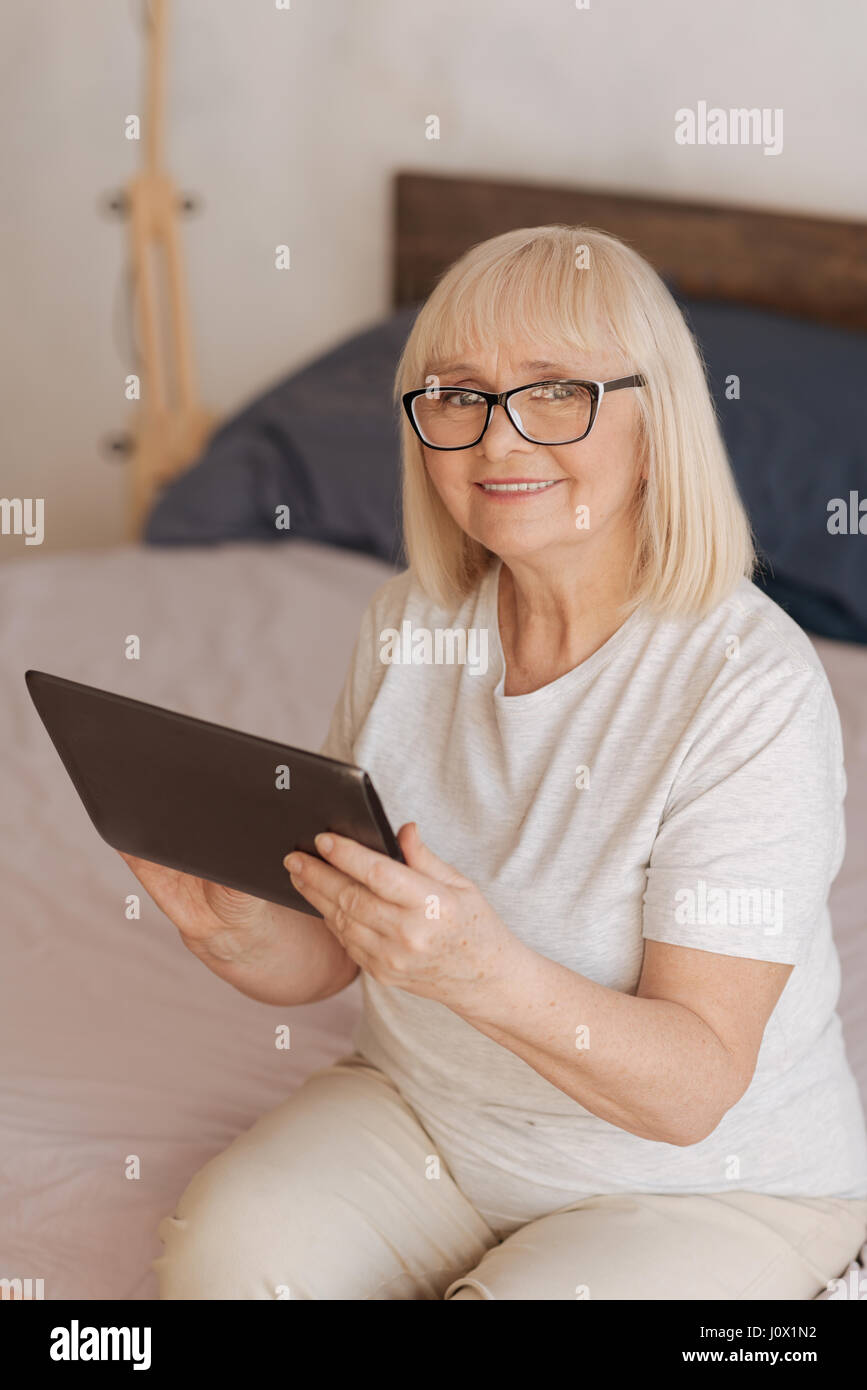 Appareil électronique portable. Bonne, à la femme âgée holding a tablet et souriant tout en en utilisant la Banque D'Images
