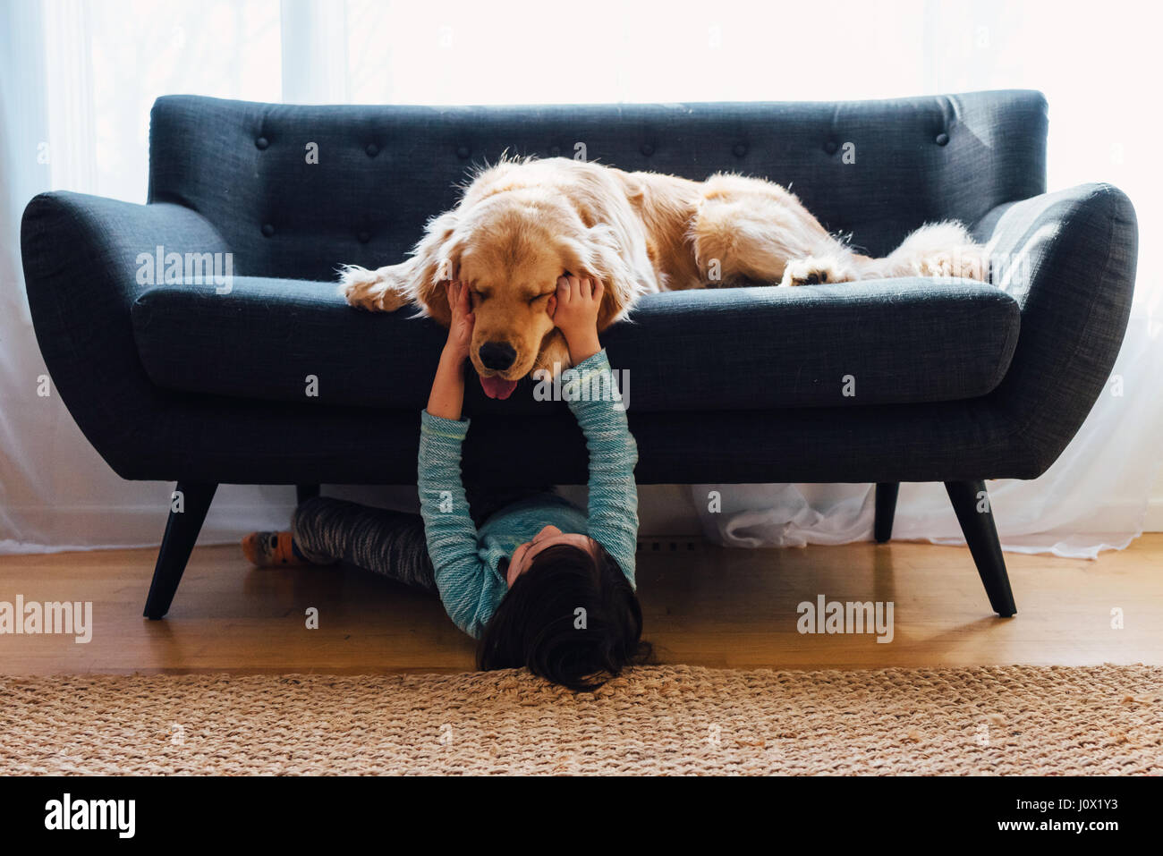 Girl lying sous canapé jouant avec son chien Banque D'Images