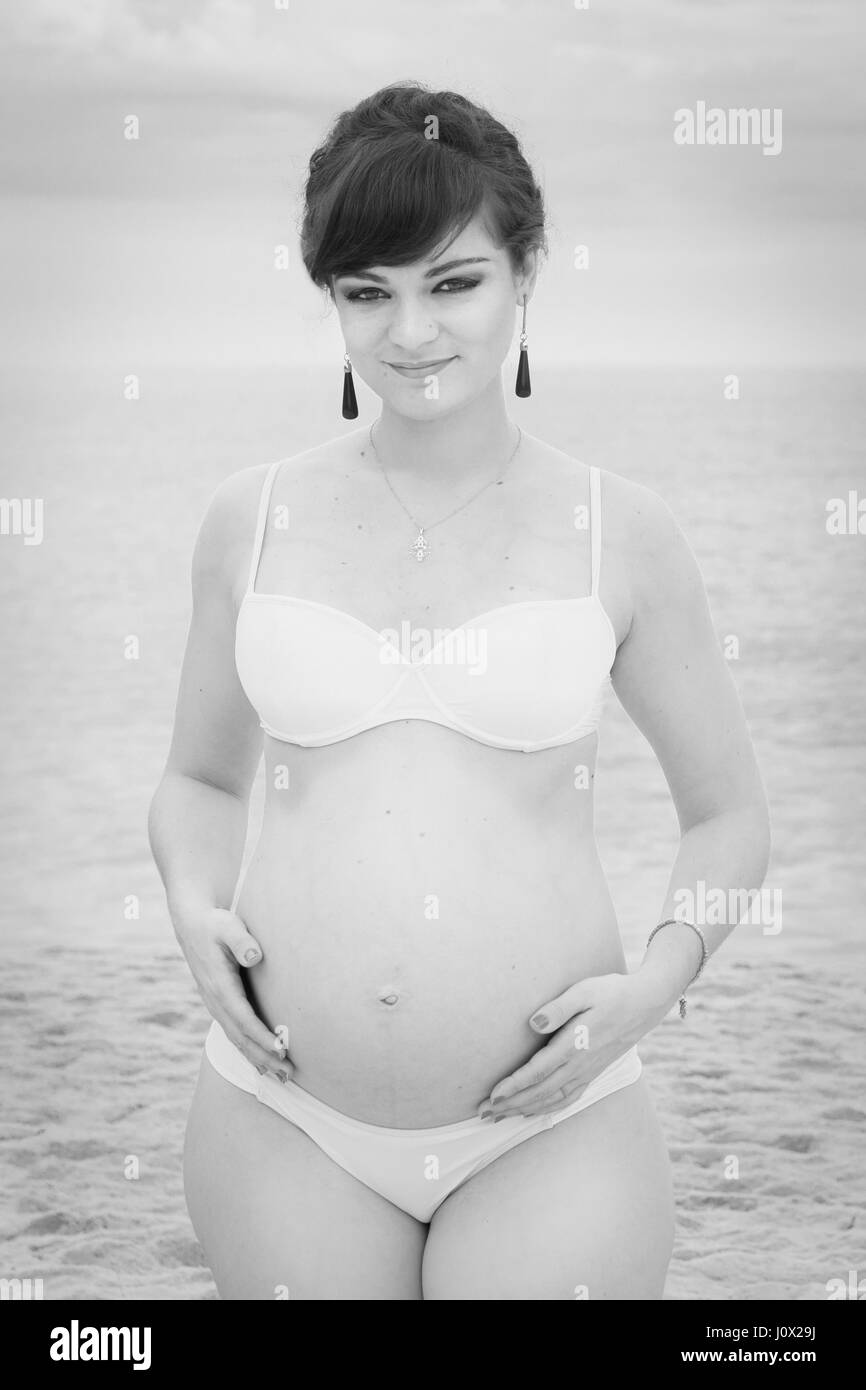 Pregnant woman Standing on beach holding her belly Banque D'Images