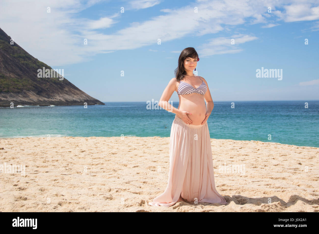 Pregnant woman sitting on beach, berçant son ventre Banque D'Images