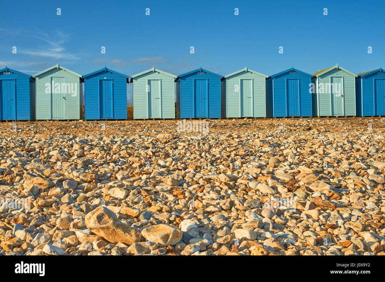 Charmouth, Dorset et une ligne de cabines de plage en alternant les couleurs bleu clair et foncé à l'arrière de la plage de galets sur un soir d'été. Banque D'Images