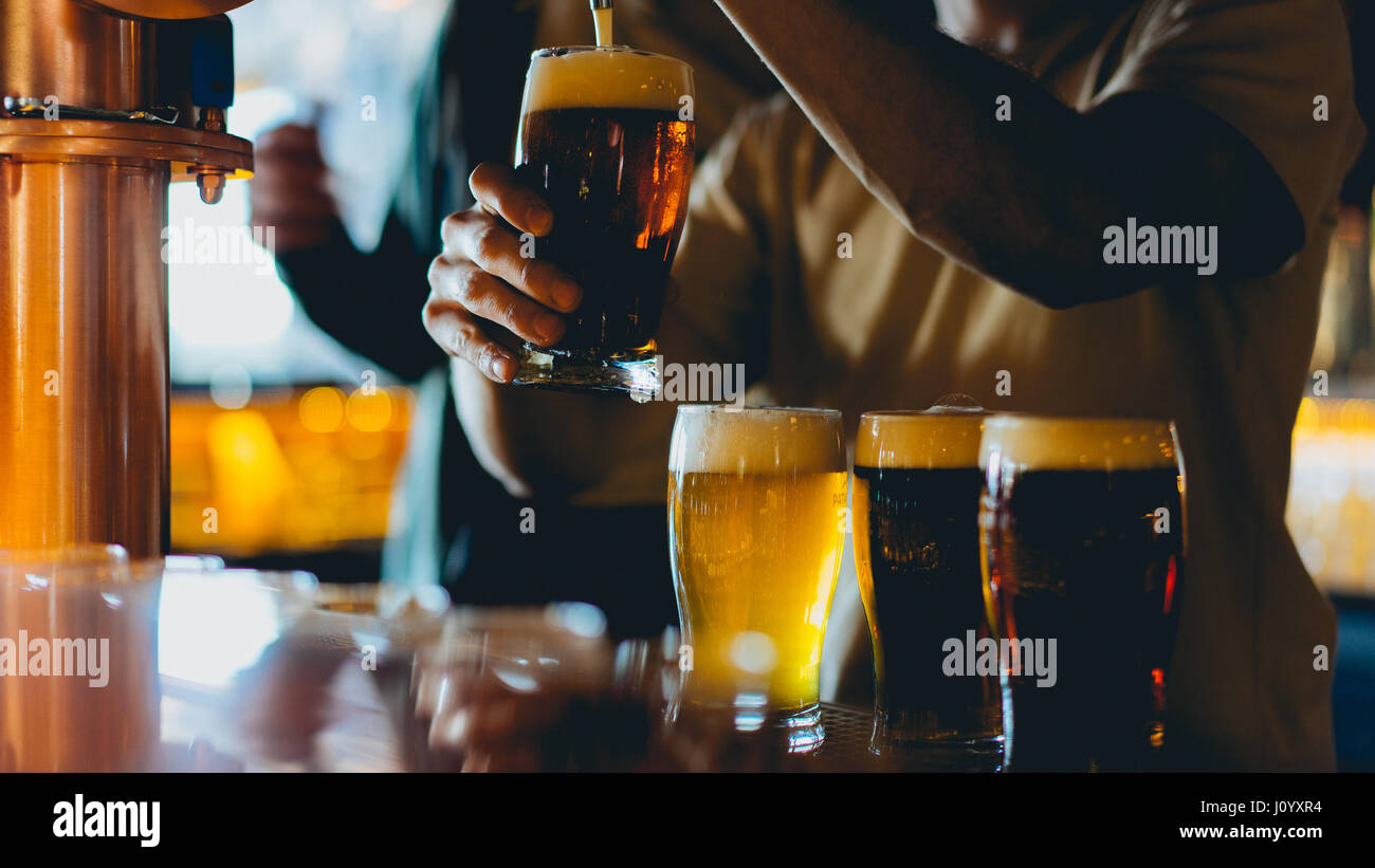 3 verres à bière complète sur un bar. 1 est comblé par un robinet. Banque D'Images