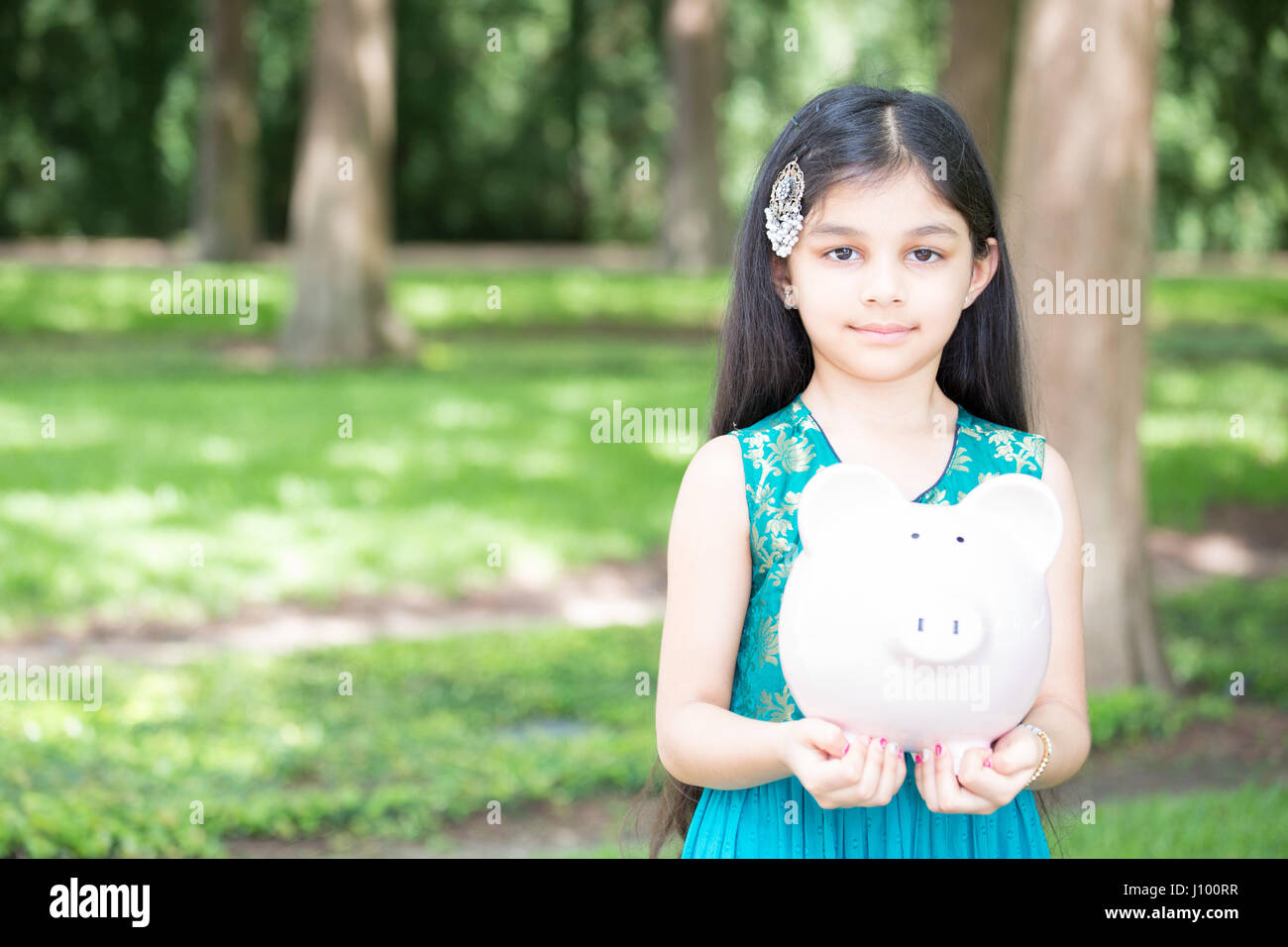 Closeup portrait, jeune dame holding piggy bank, isolé à l'extérieur de l'herbe verte et des arbres. La stratégie de l'argent Banque D'Images