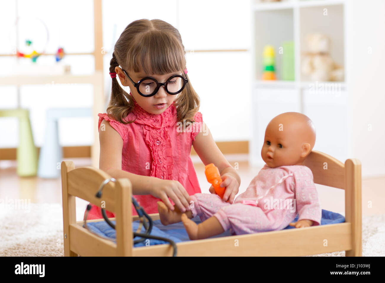 Kid enfant en maternelle ou l'école maternelle. Little girl playing doctor avec poupée. Banque D'Images