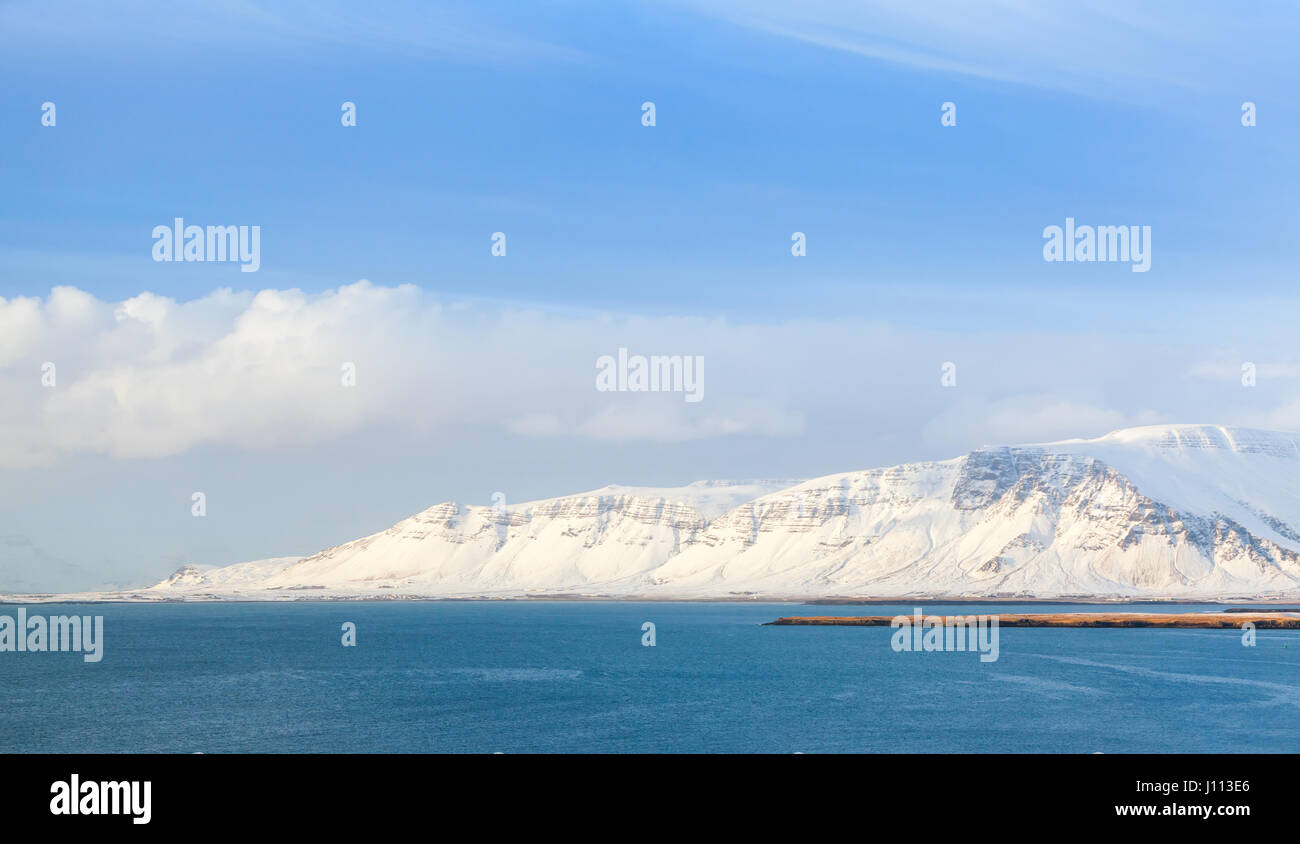 Paysage islandais côtières avec montagnes enneigées sous le bleu ciel nuageux. District de Reykjavik, Islande Banque D'Images