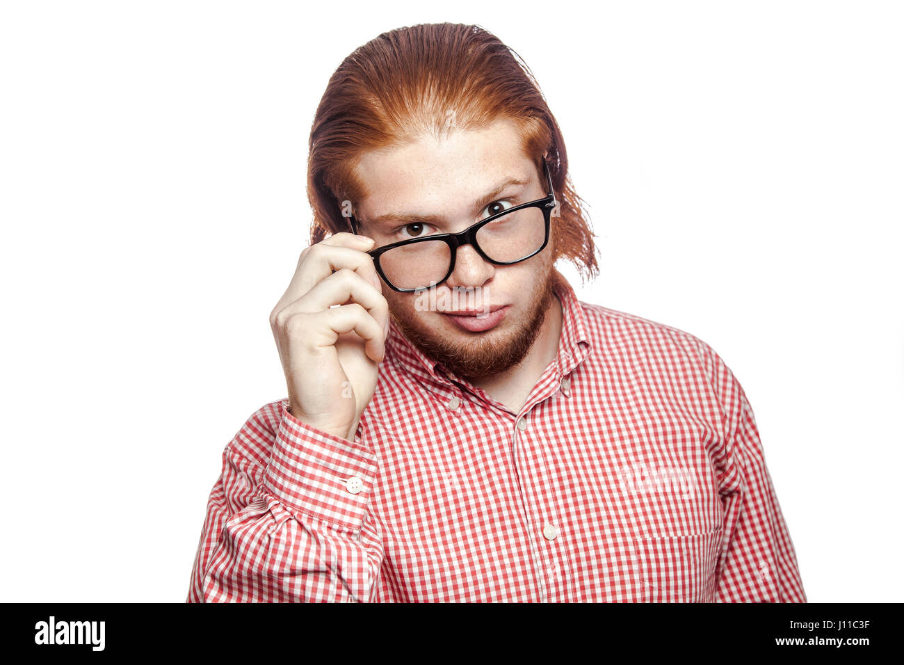 La pensée réfléchie readhead barbu businessman avec chemise rouge et de rousseur holding glasses and looking at camera . studio shot isolé sur blanc. Banque D'Images