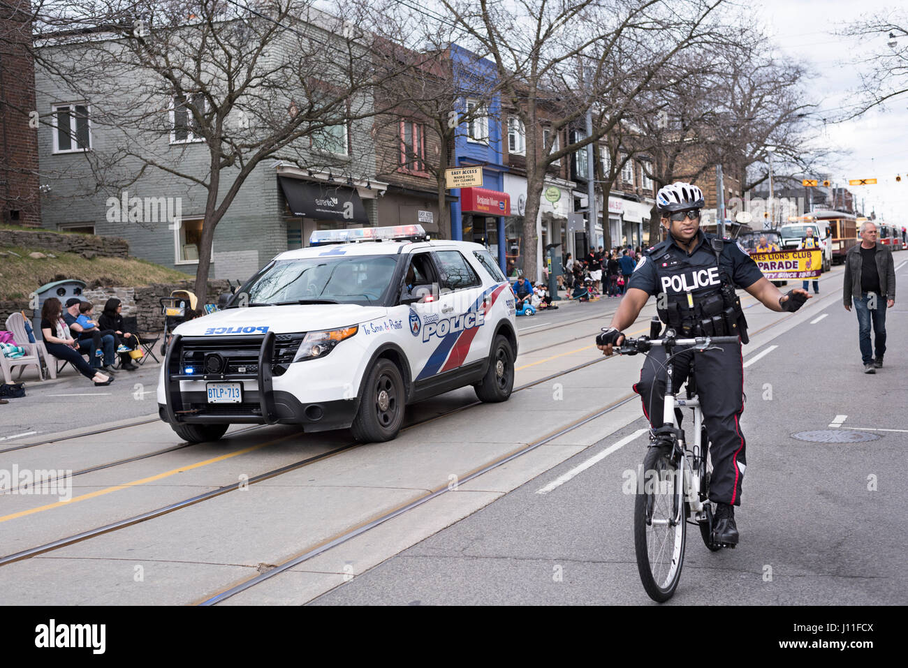 Un policier, suivi par une voiture de police, cycles au début de la parade de Pâques et des vagues de personnes le long des plages, rue Queen Toronto Banque D'Images
