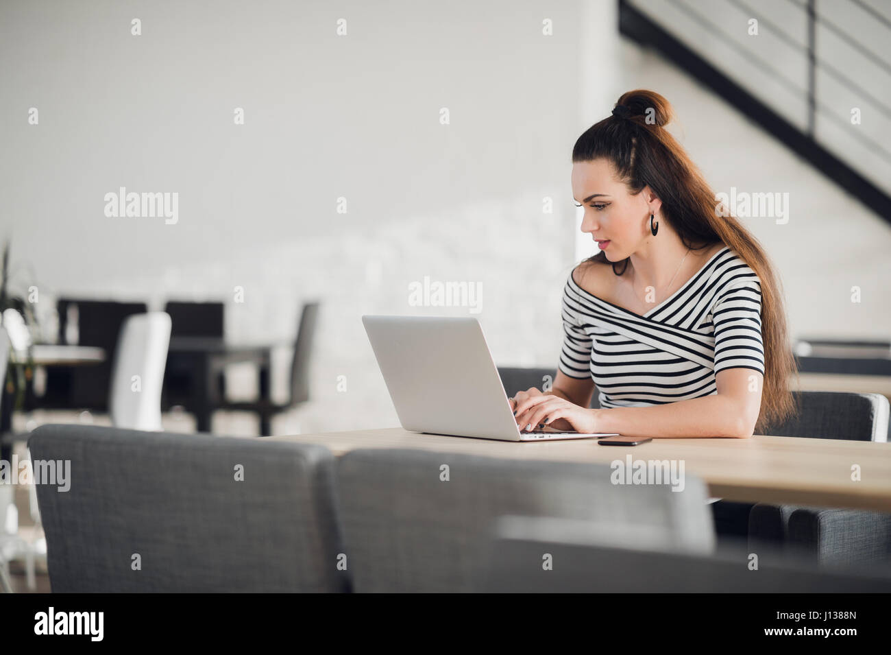 Jeune femme entrepreneur lecture livre électronique sur l'ordinateur portable pendant le déjeuner dans le restaurant moderne de l'intérieur. Businesswoman chatting on tablet élégant tout en restant assis dans un café confortable. Banque D'Images