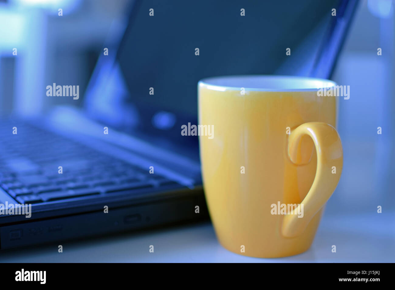 Tasse à café jaune et ordinateur portable en arrière-plan. Banque D'Images